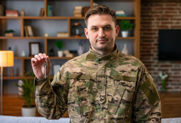 Indoor shot of military man wearing camouflage uniform and hat holding house keys, mortgage assistance from a veterans organization, extremely happy soldier male.