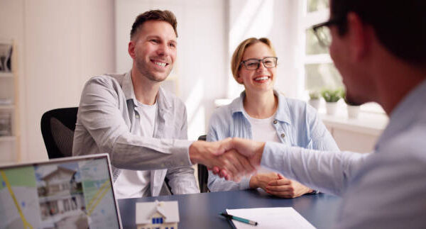 Happy Hispanic Real Estate Agent Shows House to Young Latinx Couple on Laptop at Office Desk for Mortgage Consultation.